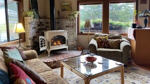 Un salon chaleureux avec une cheminée, un canapé, une table basse en verre et une vue sur l’extérieur.