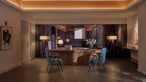 A modern hotel room with a central island, two blue chairs, a laptop, and a vase with flowers.