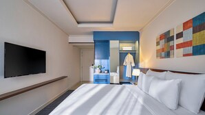 A hotel room with a large bed, a flat-screen TV mounted on the wall, a blue accent wall, and a colorful abstract painting.