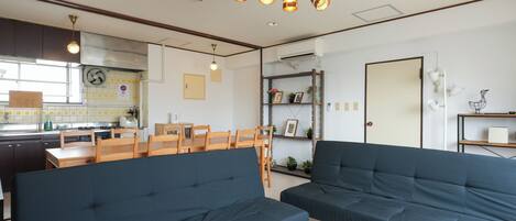 A modern living room with dark blue sofas, a dining area with wooden chairs, and a kitchen in the background.