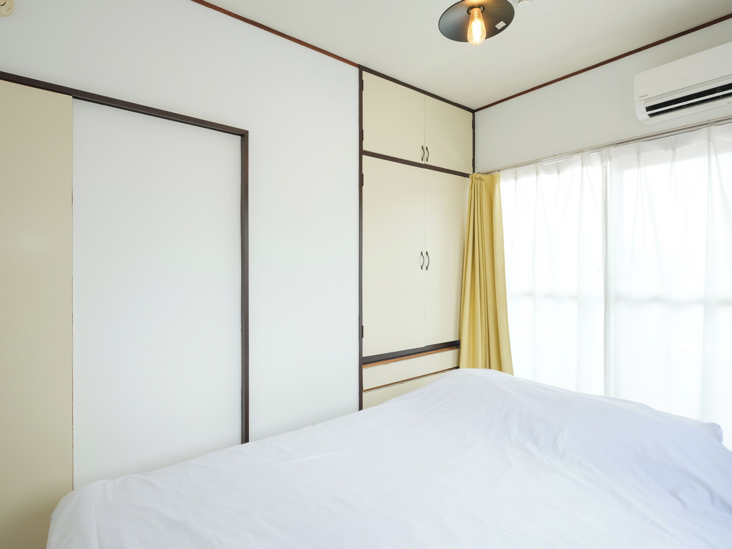 A hotel room with a bed, a wardrobe, a window with curtains, and an air conditioning unit.