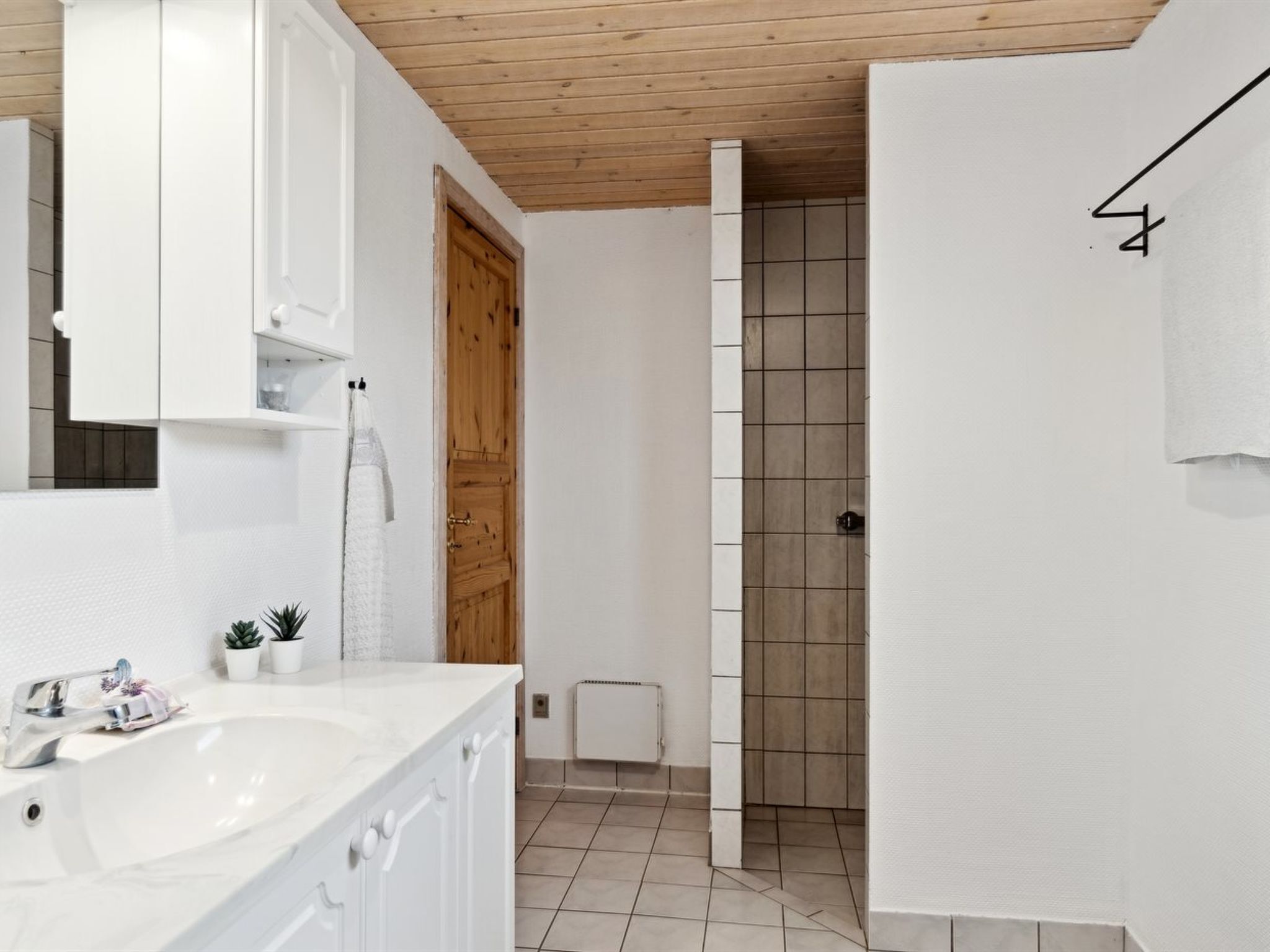 Ein modernes Badezimmer mit weißen Sanitärobjekten, einer Holztür und einem gefliesten Duschbereich.