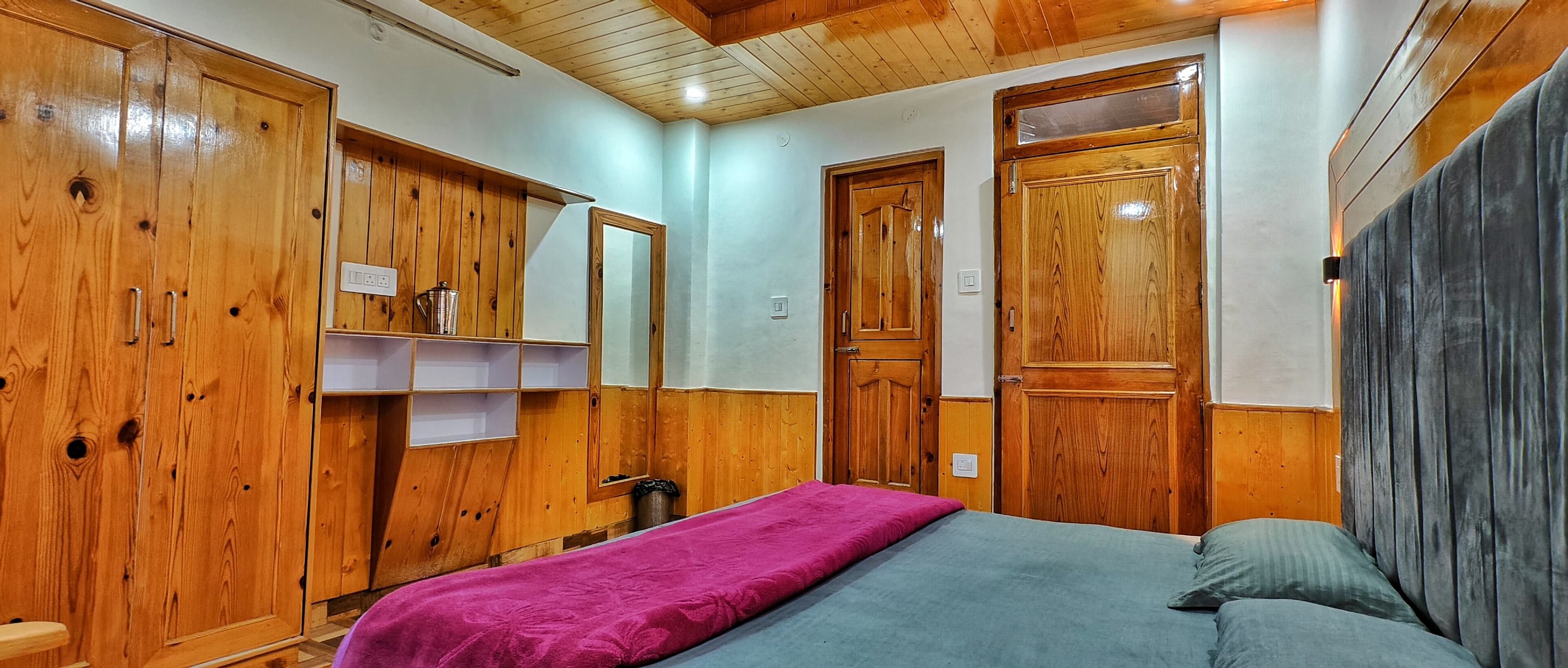 A bedroom with wooden wardrobes, a bed with a pink and blue blanket, and a grey headboard.