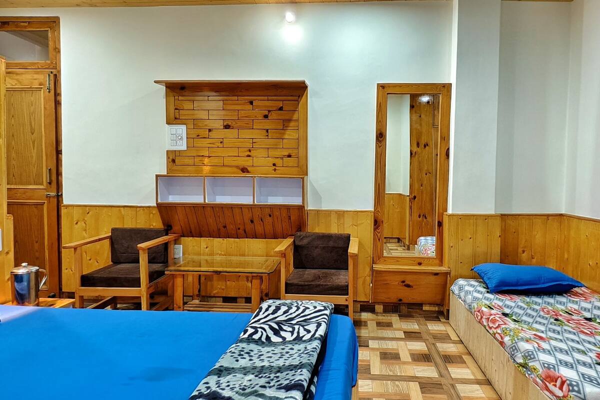 A compact room with two beds, a wooden desk, a chair, and a small kitchenette.