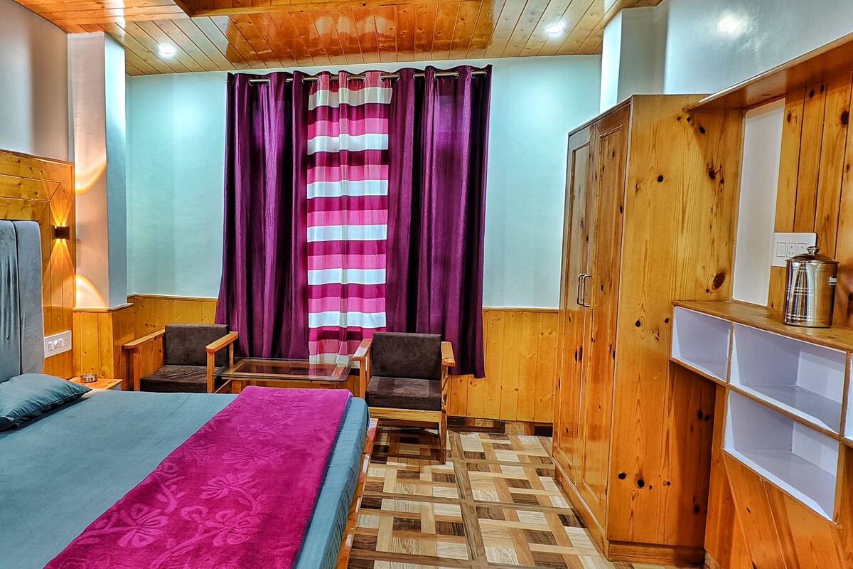 A room with a bed, a chair, a small table, a wooden wardrobe, and a window with curtains.