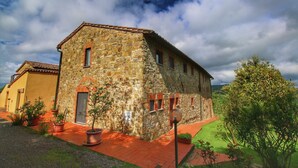 A stone building with a red-tiled roof, surrounded by potted plants and a red pathway. - Cottage in Tuscany with patio (Castiglione D'orcia)