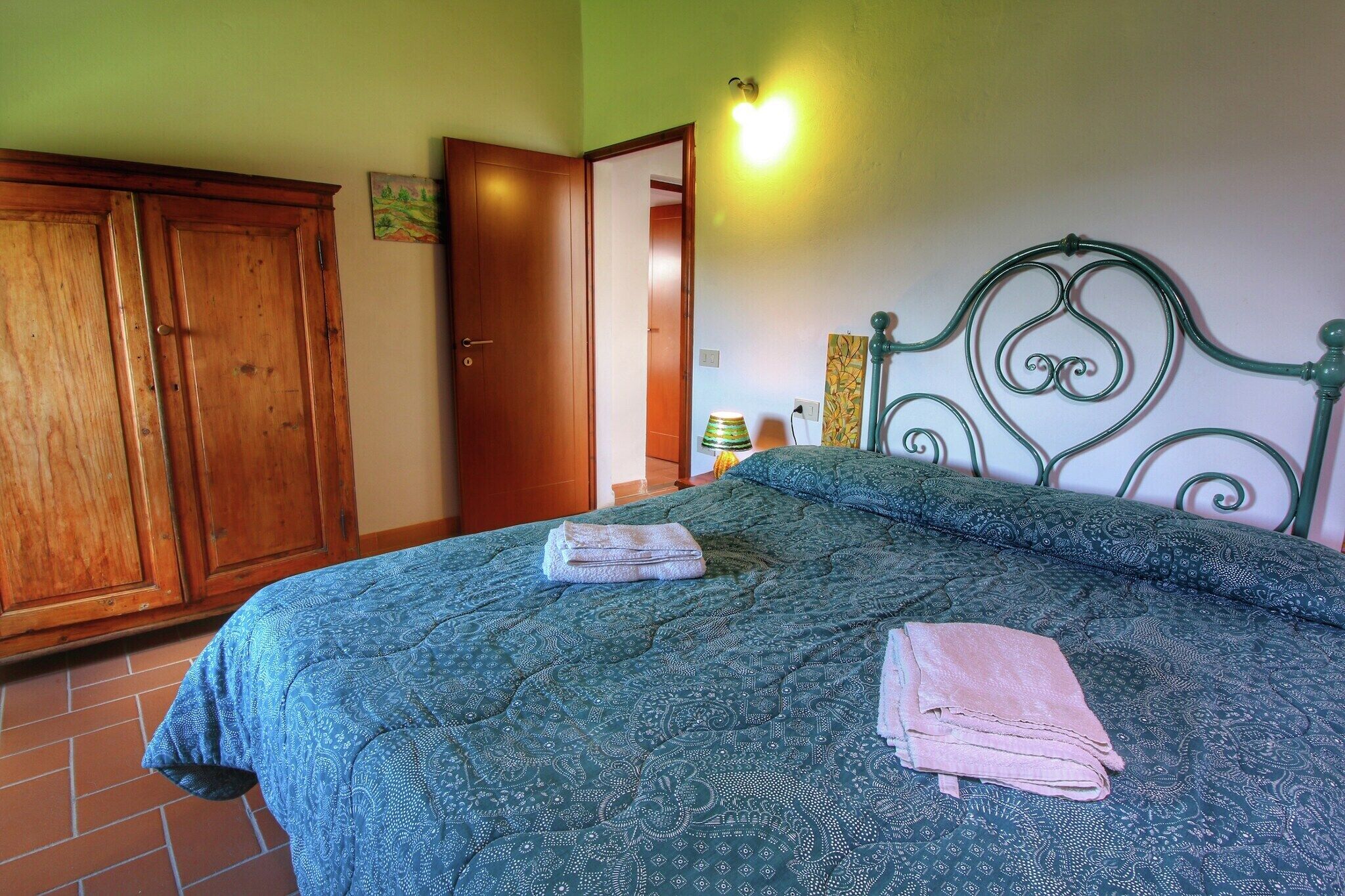A bedroom with a bed, a wooden wardrobe, and a door leading to another room.