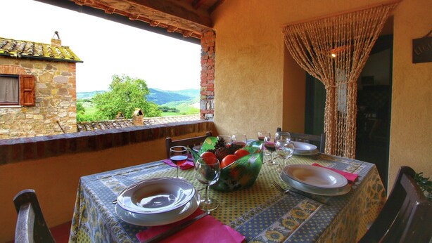 A dining table set with plates, glasses, and a fruit basket, overlooking a scenic view. - Cottage in Tuscany with patio (Castiglione D'orcia)