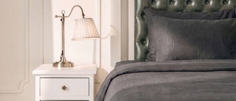Un dormitorio con cama, mesita de noche con lámpara, una silla y un cuadro en la pared.