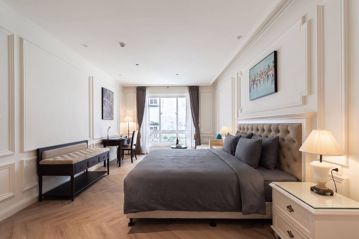 A bedroom with a large bed, a bench, a desk, and a nightstand with lamps.