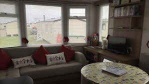 A living room with a sofa, a round table, and a television on a stand. - SeaSalt -Low cost accommodation, Harlyn Sands (Padstow)