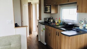 A compact kitchen with wooden cabinets, a microwave, a toaster, and a small refrigerator. - SeaSalt -Low cost accommodation, Harlyn Sands (Padstow)