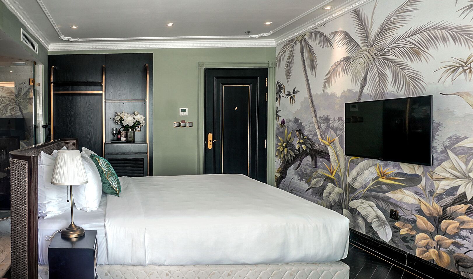 A hotel room with a large bed, a TV mounted on the wall, and a tropical-themed mural.