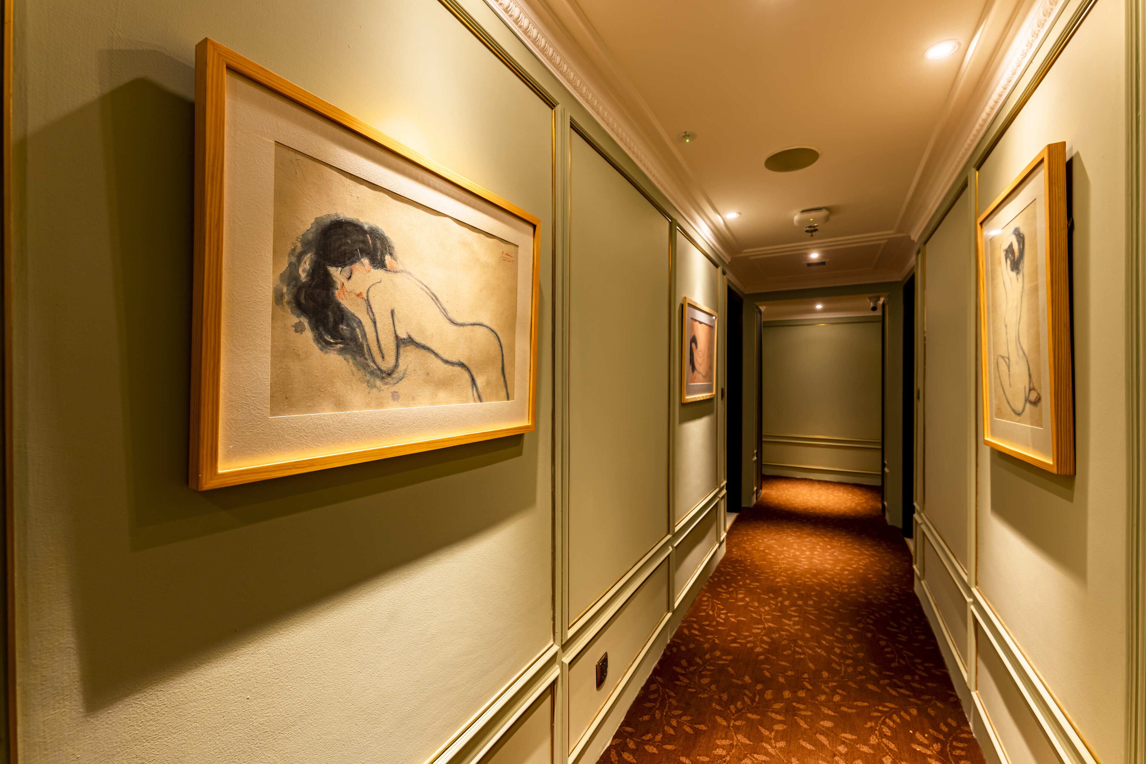 Un couloir aux murs ornés de tableaux encadrés, doté d’un sol recouvert de moquette et terminé par une porte.