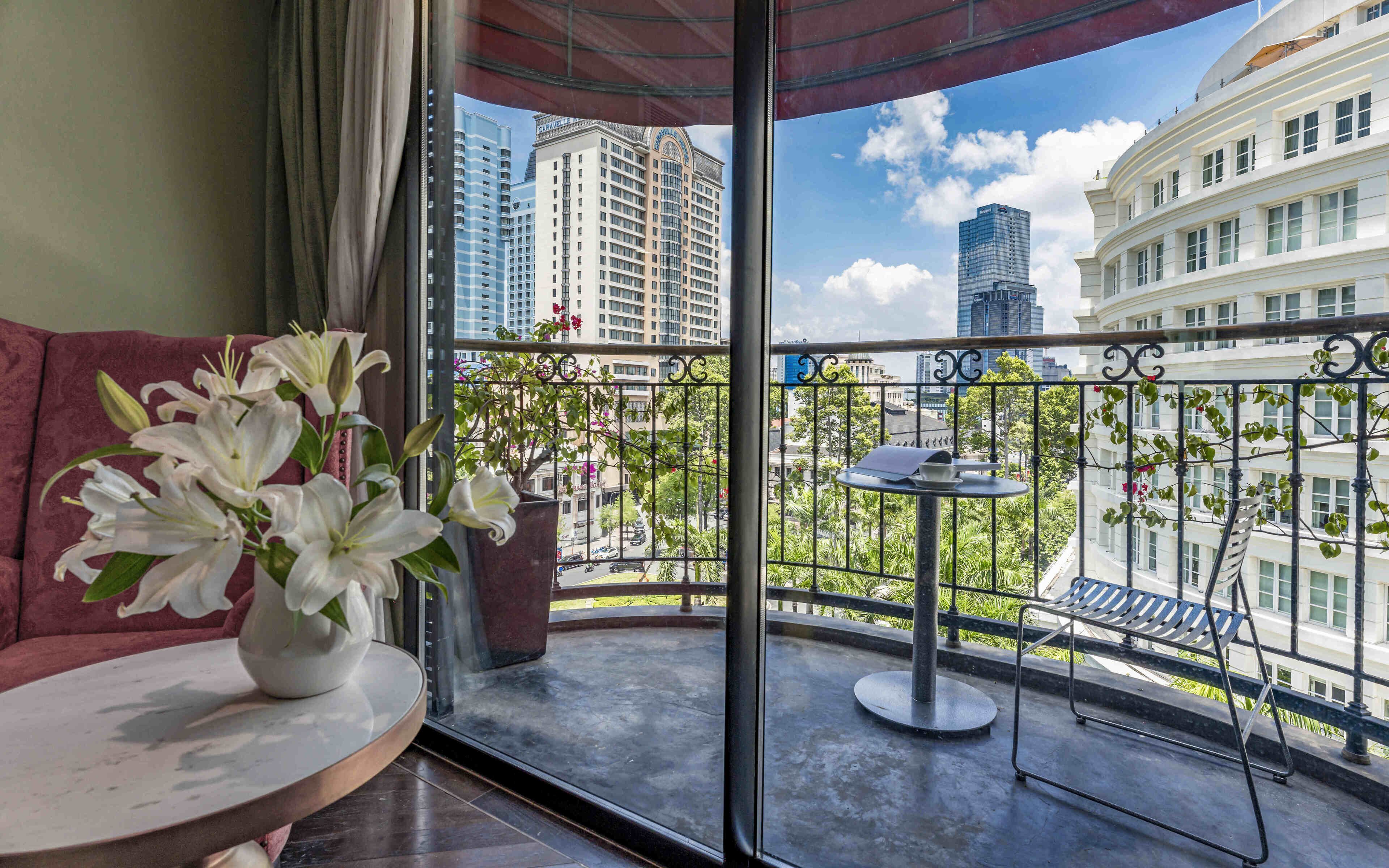 A balcony with a view of tall buildings, a round table with a vase of flowers, and a metal chair.