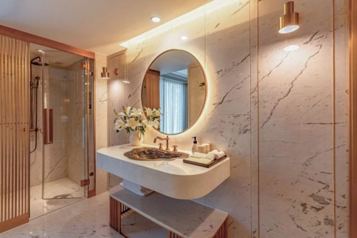 Un baño moderno con tocador de mármol, un espejo redondo y zona de ducha.