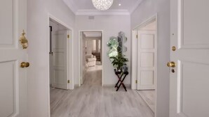 A hallway with white doors, a chandelier, and a potted plant.