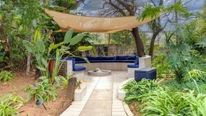 An outdoor seating area with a fire pit, surrounded by lush greenery and a canopy.