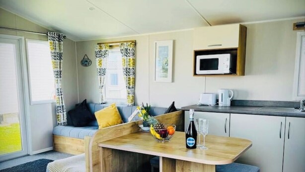Un espacio habitable pequeño con kitchenette, zona de estar con cojines y mesa de comedor con frutero y botella.