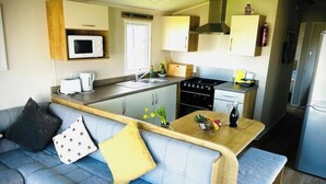 Cocina compacta con microondas, estufa y pileta. Hay un sofá azul con almohadones y una mesa de madera con una piña y flores.