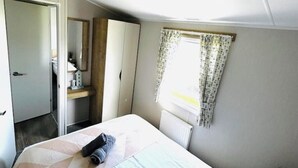 Un dormitorio con cama, armario, una mesita de noche con lámpara y una ventana con cortinas.