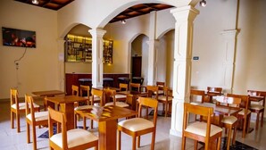 A dining area with multiple wooden tables and chairs, white pillars, and a bar area in the background.