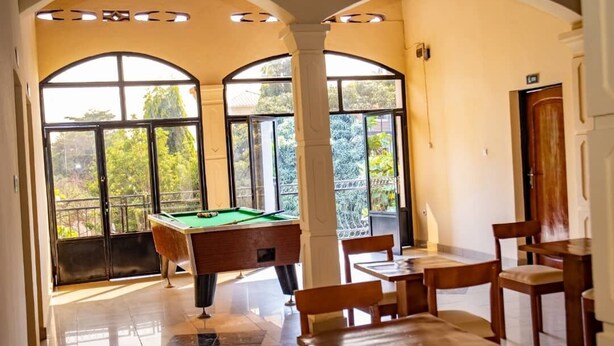 A pool table in a room with large windows and a dining area.