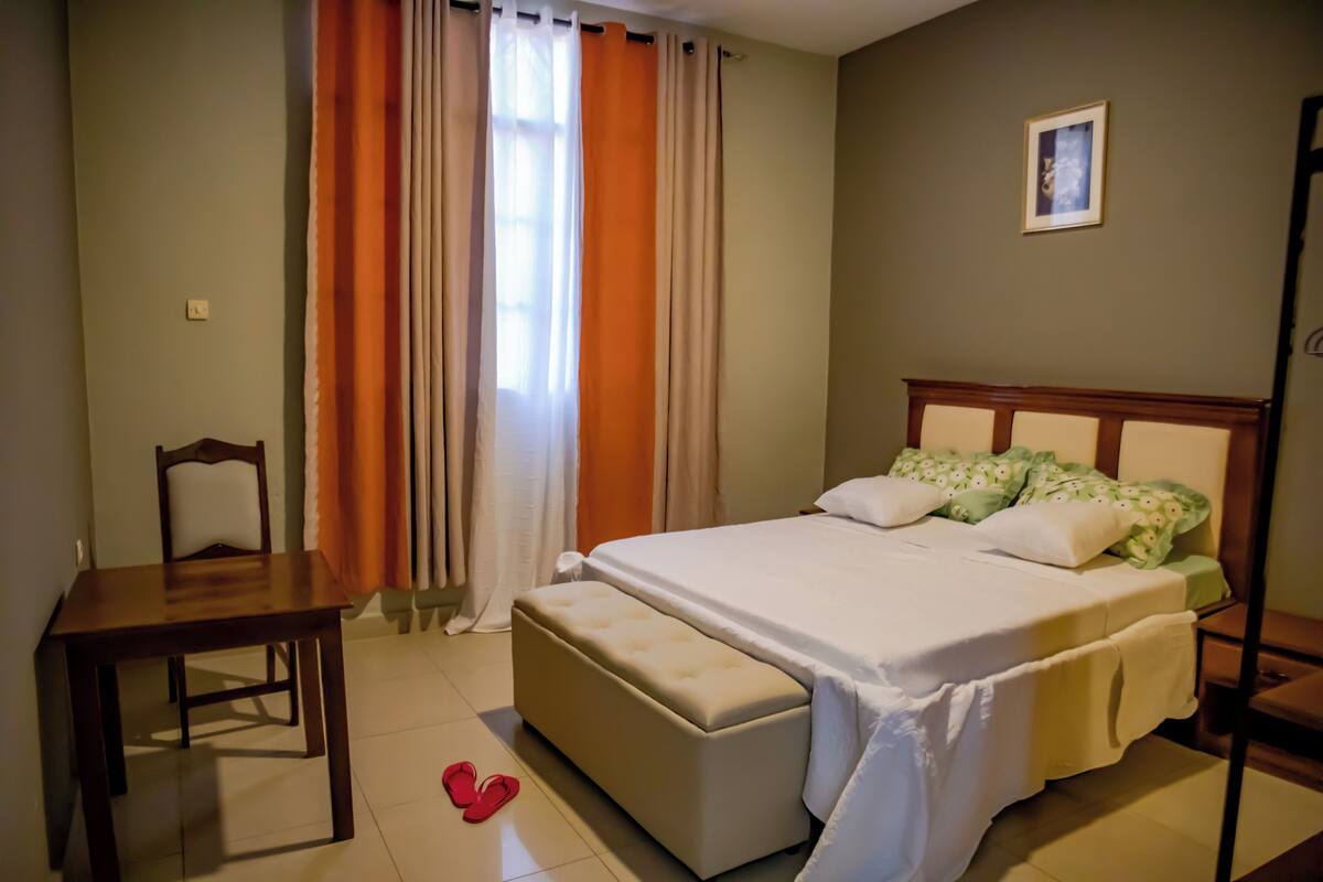 A bedroom with a bed, a wooden nightstand, a chair, and a bench.