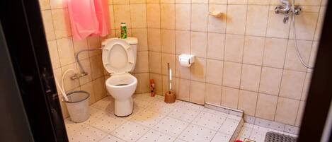 A bathroom with a toilet, bidet, shower, and a pair of red slippers on the floor.