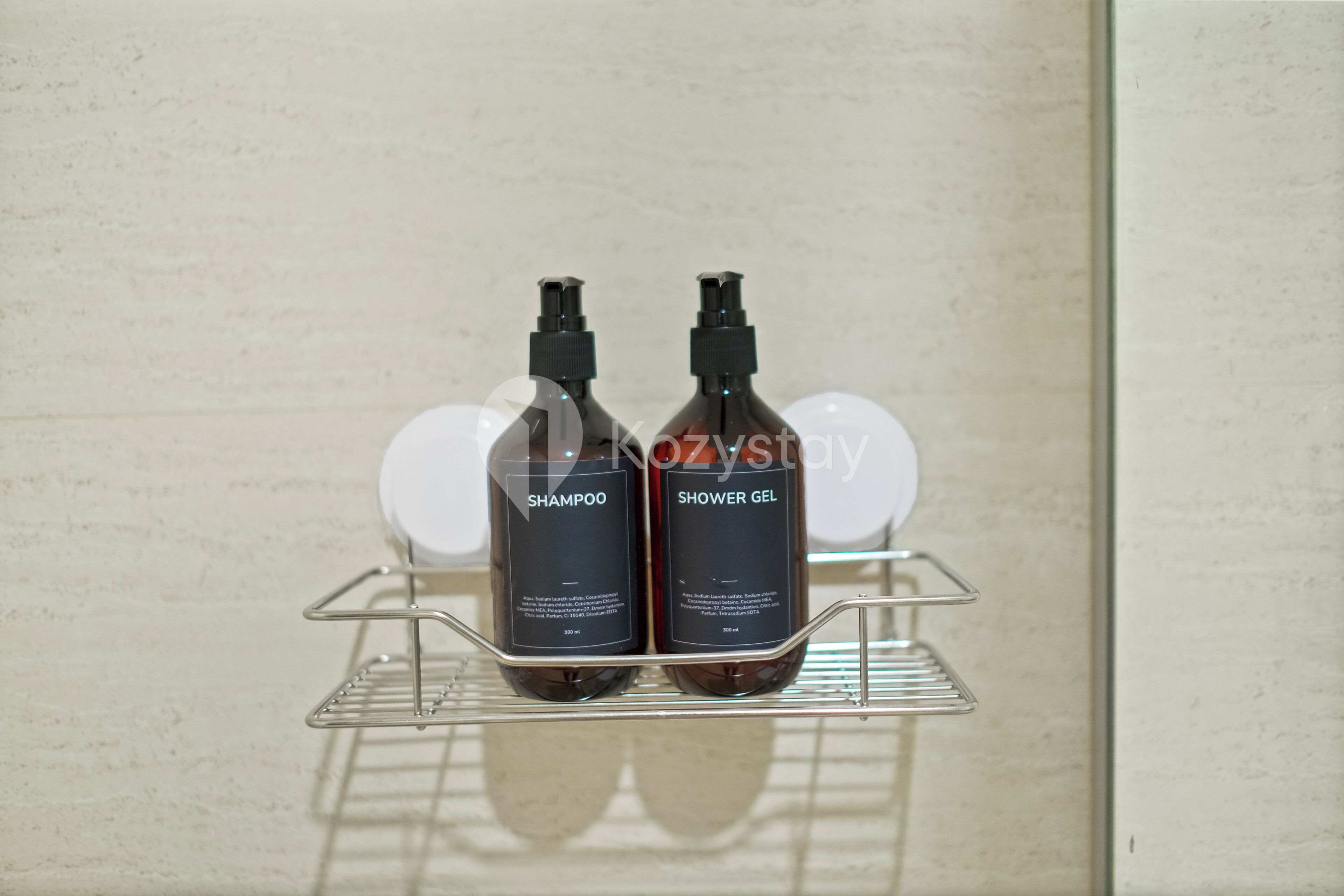 Dos botellas de champú y gel de ducha sobre una rejilla metálica apoyada en una pared.