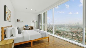 A modern bedroom with a large window, wooden floor, and a city view.