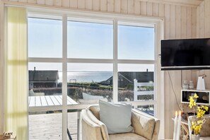 A room with a large window, a TV, and a chair with a cushion. - Lovely holiday home with sea view (Faaborg)