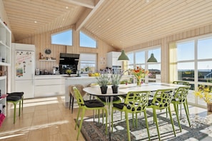 A spacious kitchen with wooden ceiling, large windows, and a dining area with green chairs and a table. - Lovely holiday home with sea view (Faaborg)