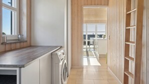 Een moderne keuken met een ingebouwde wasmachine, houten lambrisering en uitzicht op een buitenruimte.