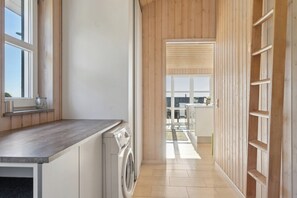 A modern kitchen with a washing machine, wooden walls, and a view to a balcony. - Lovely holiday home with sea view (Faaborg)