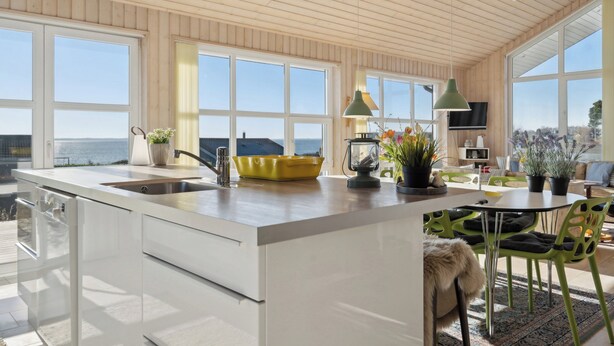 Een moderne keuken met een groot schiereiland, een eethoek met groene stoelen en uitzicht op zee.