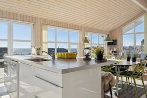 A modern kitchen with a large island, a dining area with green chairs, and a view of the sea. - Lovely holiday home with sea view (Faaborg)
