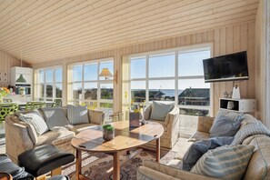 A spacious living area with a large window, a flat-screen TV, and a dining table. - Lovely holiday home with sea view (Faaborg)