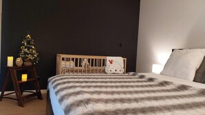 A bedroom with a wooden crib, a small Christmas tree, and a bedside table with candles. - El Nido BY LAVILLA25 Noaillan (Noaillan)