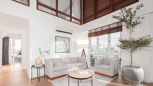 Una sala de estar moderna con un sofá gris, una mesa de centro redonda y una gran planta en maceta.