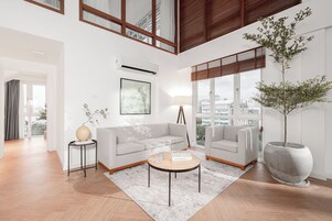 Una sala de estar moderna con un sofá gris, una mesa de centro redonda y una gran planta en maceta.