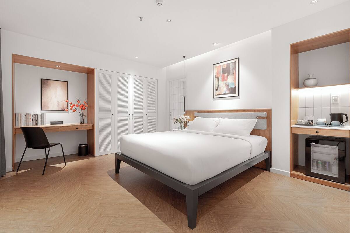 A modern bedroom with a bed, a desk, and a kitchenette.