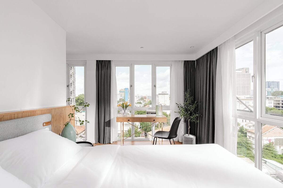 A modern hotel room with a large bed, a desk, and a view of the city.