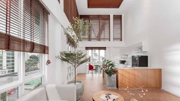 Un interior moderno con sala de estar, cocina y comedor. Hay ventanas grandes con persianas, un sofá, una mesa de centro y una encimera de cocina.