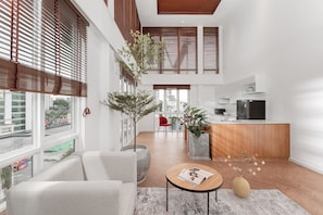 A modern interior with a living area, kitchen, and dining space. There are large windows with blinds, a sofa, a coffee table, and a kitchen counter. - M Village Hotel Hai Bà Trưng, a brand of Modern Village Lifestyle (Ho Chi Minh City)