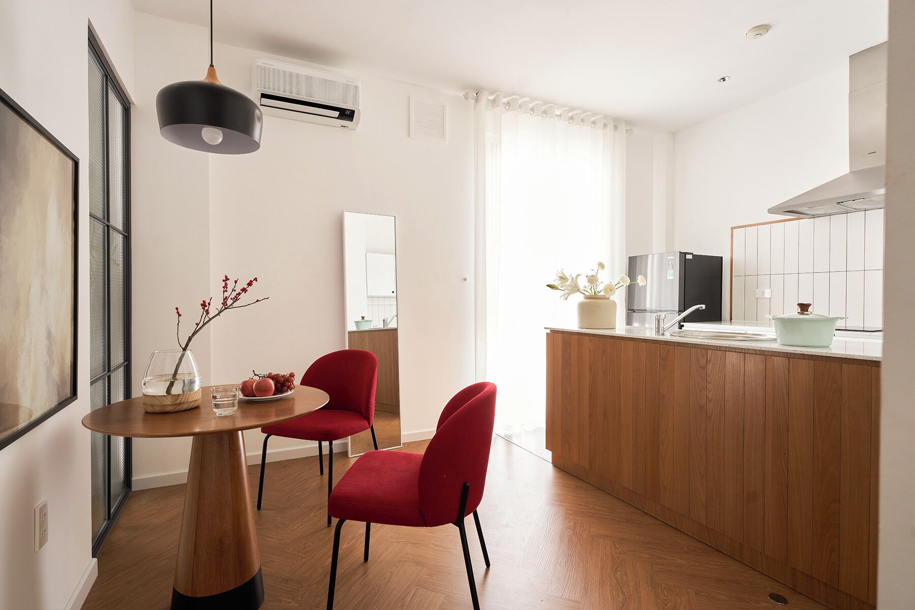 Une cuisine moderne avec des meubles en bois, un réfrigérateur en acier inoxydable et un évier. On y trouve également un coin repas avec une table en bois et deux chaises rouges.