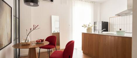 Une cuisine moderne avec des meubles en bois, un réfrigérateur en acier inoxydable et un évier. On y trouve également un coin repas avec une table en bois et deux chaises rouges.