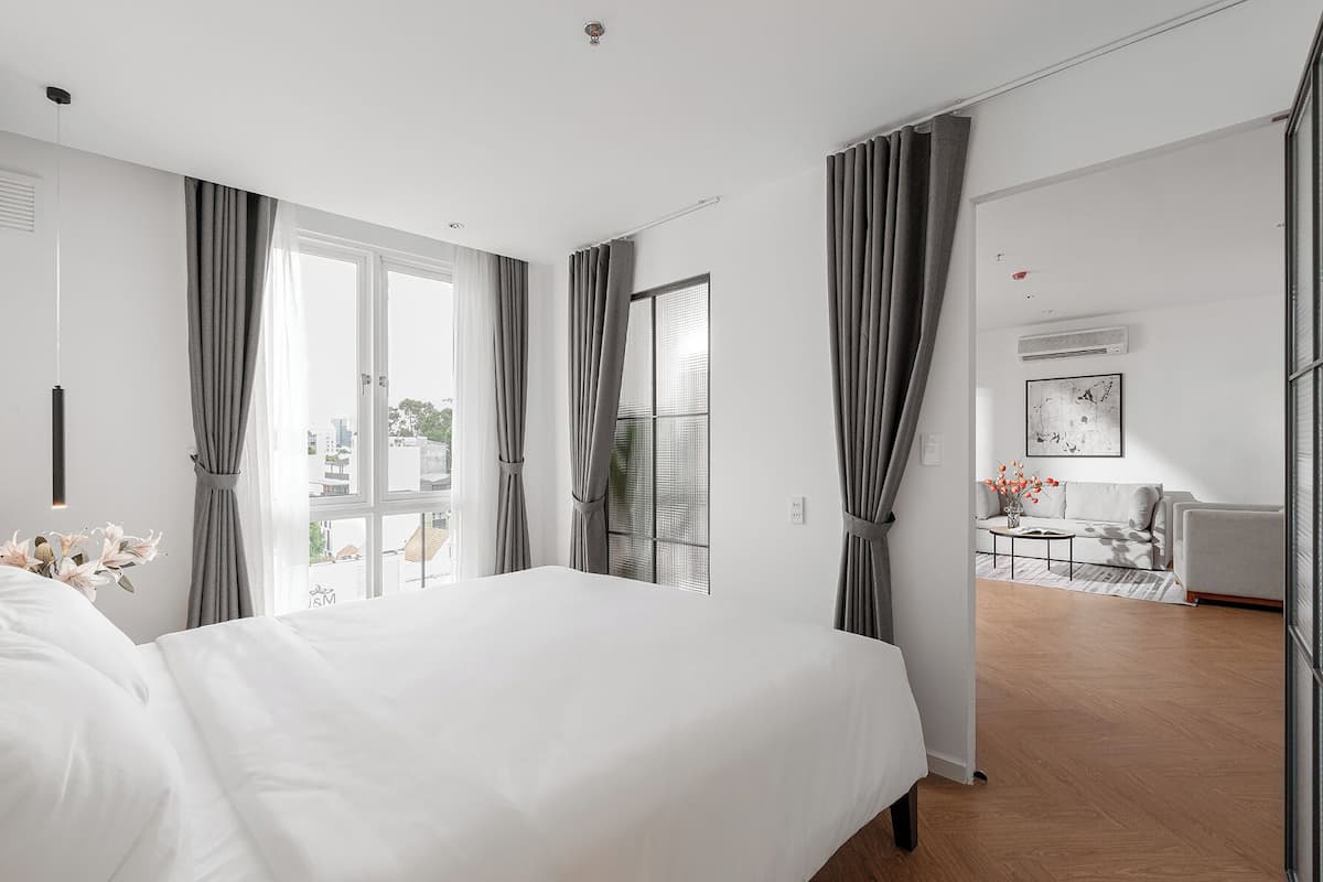 A modern hotel room with a large bed, a sitting area with a sofa and coffee table, and a view of the city through large windows.