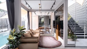 Una sala moderna con un sofá, una mesa de centro y una planta en maceta. Hay una puerta de cristal que da a un balcón con piscina.