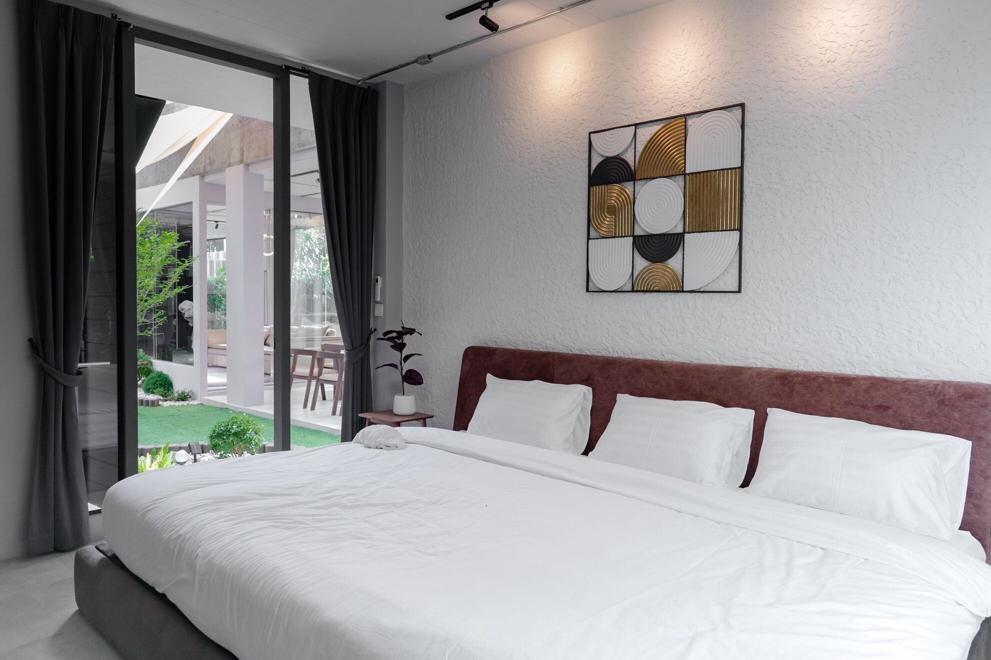 A hotel room with a large bed, a view of the outdoors, and a modern wall art piece.